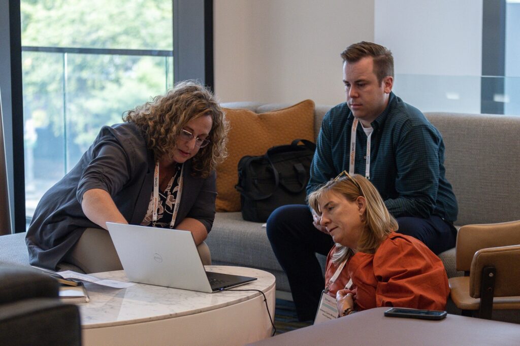 Three coworkers gather around a laptop in conversation