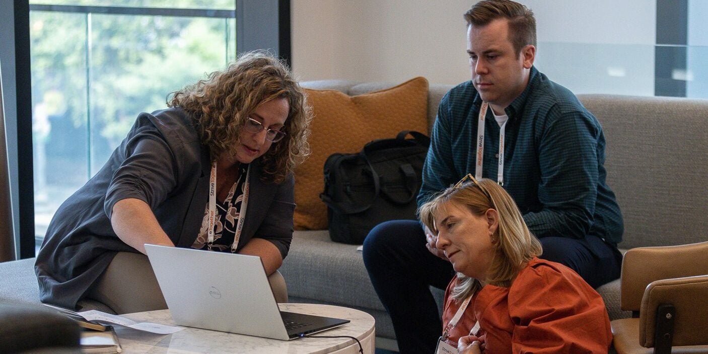 Three coworkers gather around a laptop in conversation