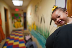 A young child smiles over an adult's shoulder