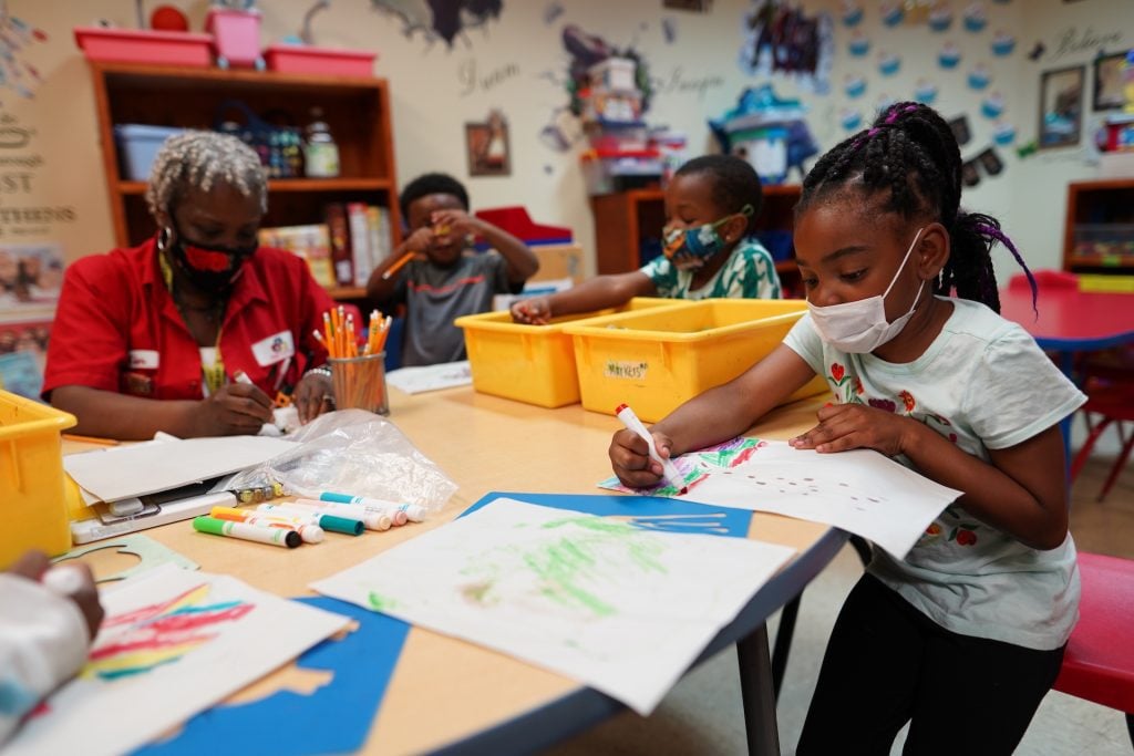 Children and an adult sit around a table coloring