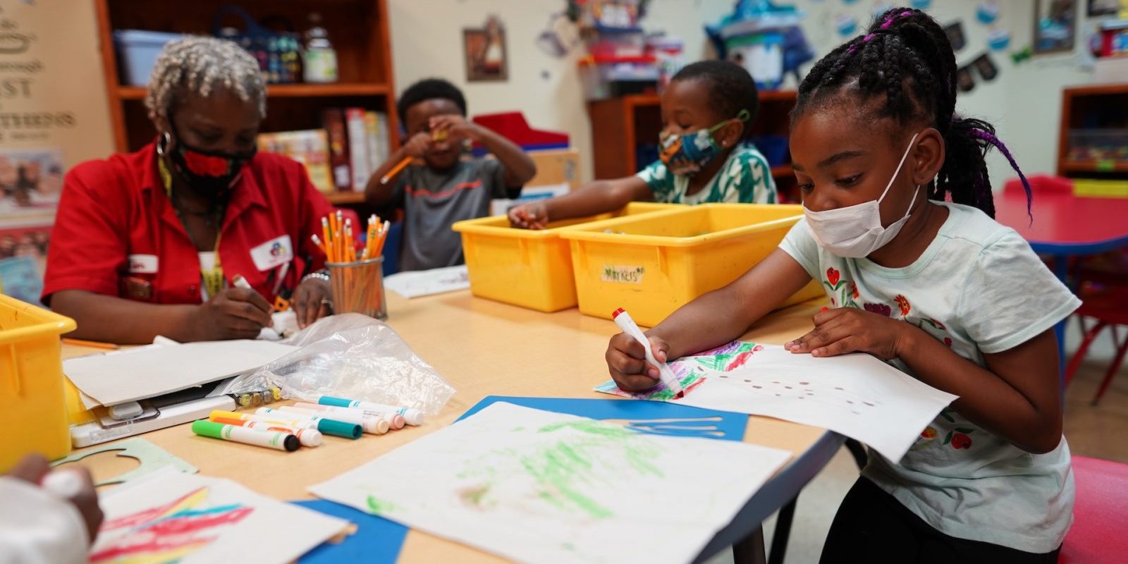 Children and an adult sit around a table coloring