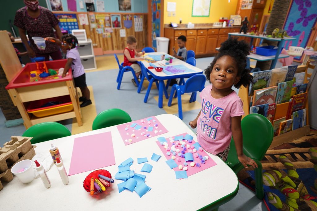 A young student smiles as she stands at a table