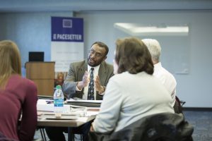 An adult speaking to others sitting around a table.