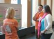 A group of three people stand discussing a timeline that's posted on the wall