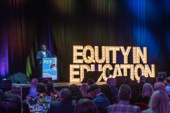 Lavert Robinson speaks at All Hands Raised' annual gala. Next to him are large letters that spell out "Equity in Education."