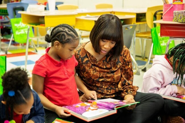 A teacher and a young girl look at a book together