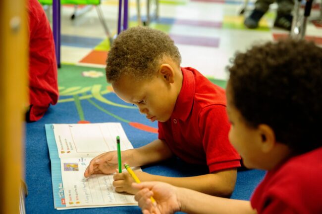 A young boy lays on the floor, practicing his writing in a workbook.