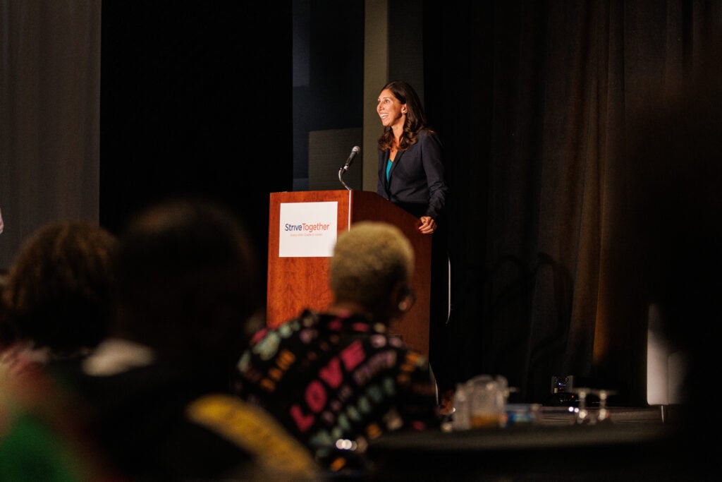 Jennifer Blatz speaks at a podium at the Cradle to Career Network Convening. The podium has the StriveTogether logo on it.