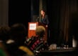 Jennifer Blatz speaks at a podium at the Cradle to Career Network Convening. The podium has the StriveTogether logo on it.