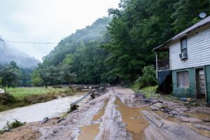 A road shows the impact of the 2022 flood in Eastern Kentucky. It is still filled with water and a home alongside it has suffered flood damage.