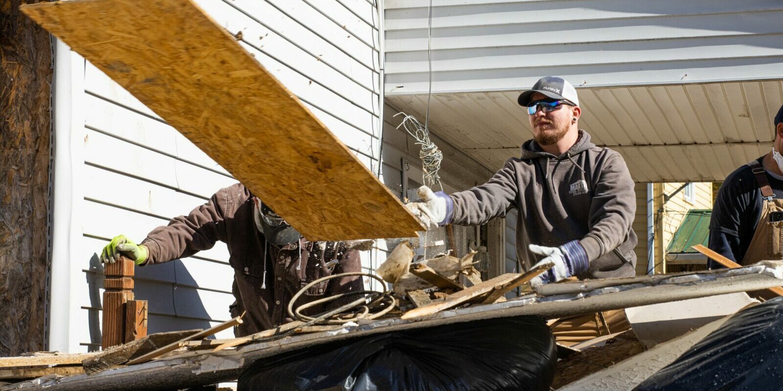 A young man is helping with disaster relief after historic flooding in southeastern Kentucky in 2022. He's tossing a piece of plywood on to a pile of debris.