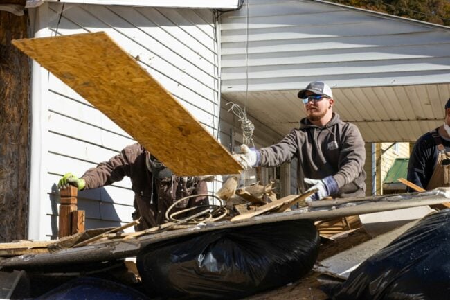 A young man is helping with disaster relief after historic flooding in southeastern Kentucky in 2022. He's tossing a piece of plywood on to a pile of debris.