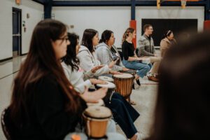 A group of people sit in a circle, playing drums.