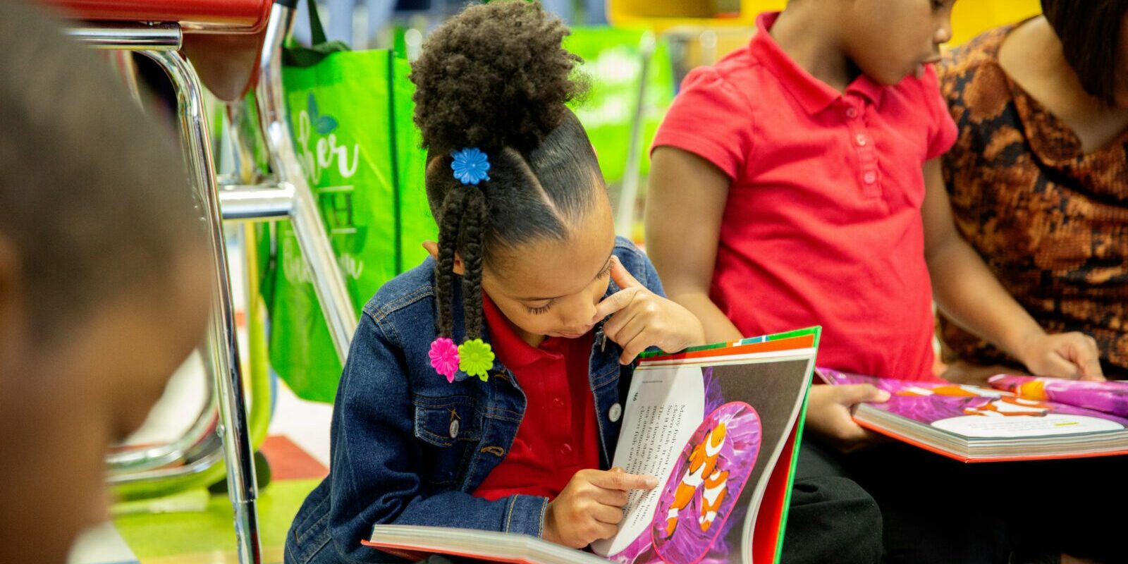 A young girl sits on the ground, reading a book she's holding in her lap.