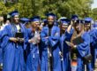 A group of six high school graduates are wearing their caps and gowns and smiling at the camera.