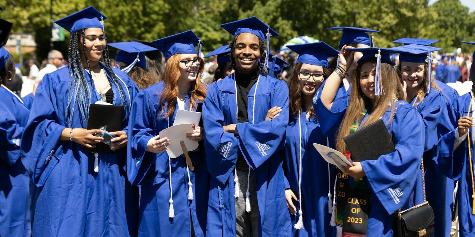 A group of six high school graduates are wearing their caps and gowns and smiling at the camera.