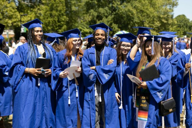 A group of six high school graduates are wearing their caps and gowns and smiling at the camera.