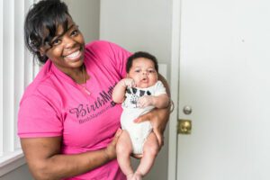 A woman holds an infant up to the camera, smiling widely.