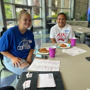 Two students sit at a table, smiling at the camera.