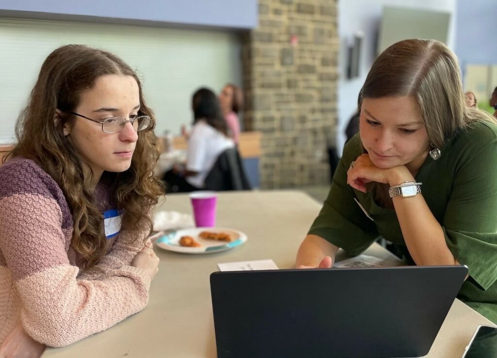 A student and a school staff member look at a laptop together.