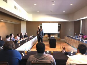 A group of youth sit around a table, listening to a man present an essential skills workshop for the hospitality sector.