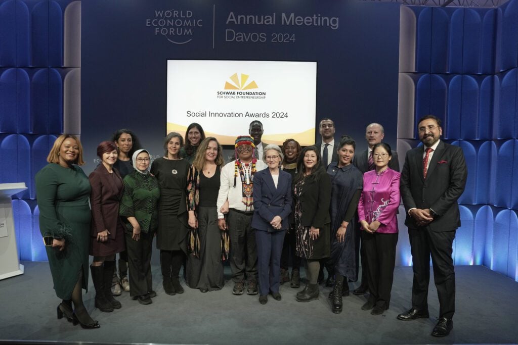 The recipients of the Schwab Foundation 2024 Social Innovation Awards stand on a stage, smiling at the camera