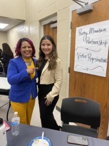 Two women smile at the camera, next to a handwritten sign that reads "Rocky Mountain Partnership Voter Registration"