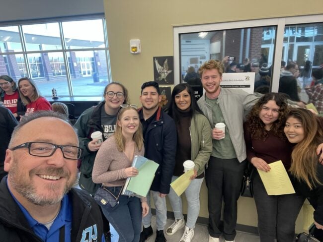 A group of eight people pose for a selfie, all smiling at the camera.