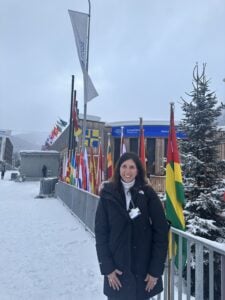 Jennifer Blatz stands outside the Congress Centre, where the World Economic Forum is hosted. She's wearing a winter coat and standing in front of a line of flags from different countries.