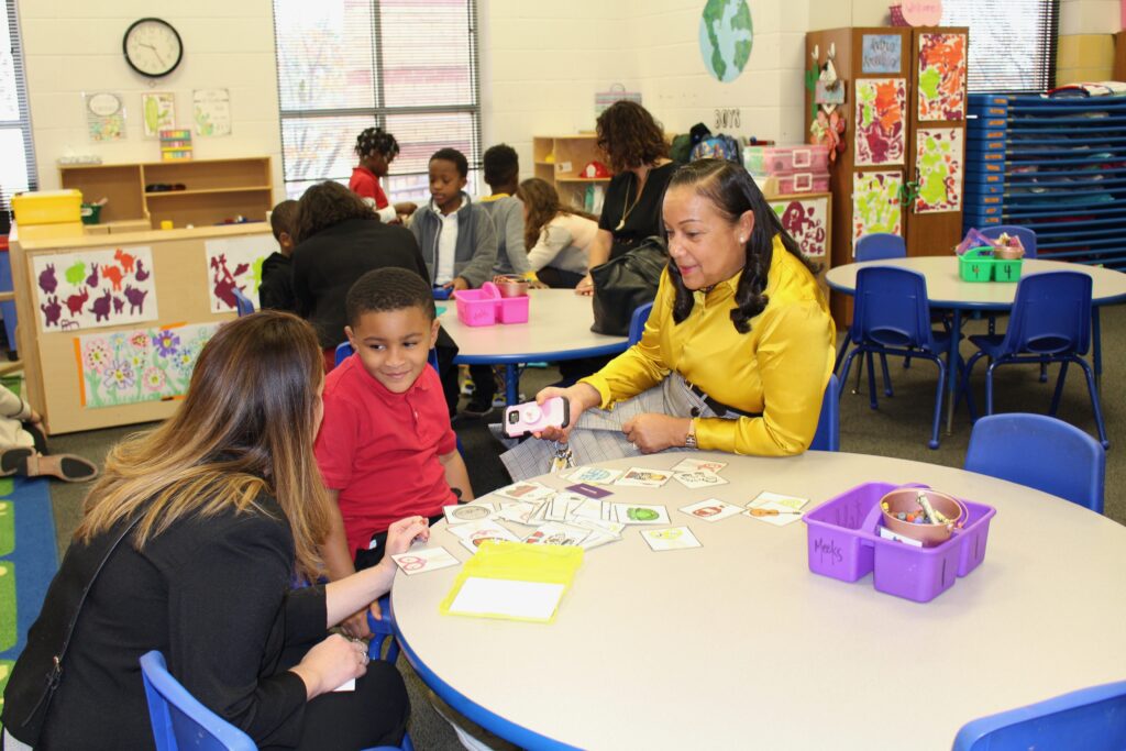 Two adults sit at a table with a young student, who's learning using flash cards.