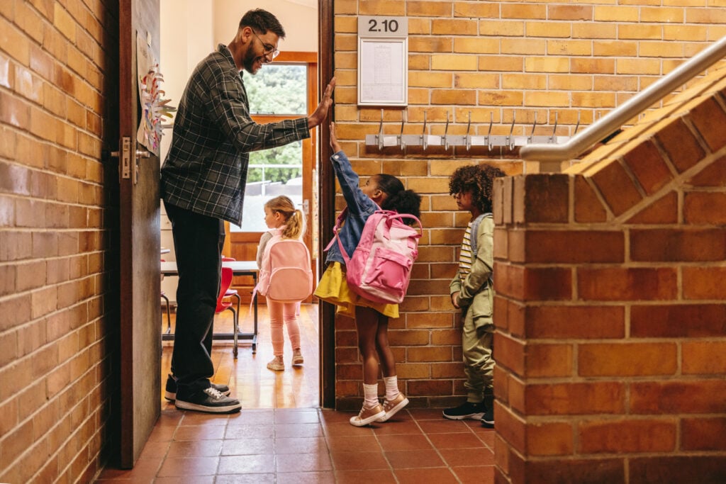 Male teacher welcoming his class with a high five outside their classroom.