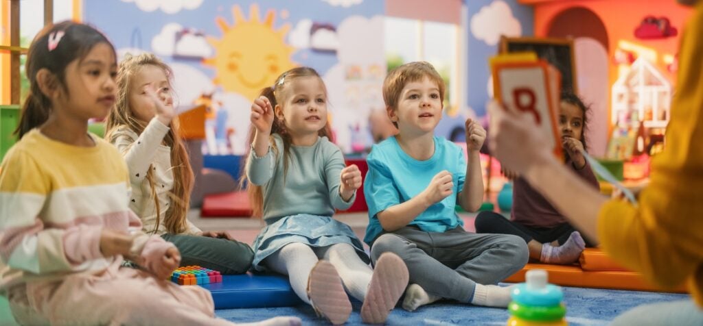 Cheerful Preschool Educator Playing and Creatively Studying with Multiethnic Kids in Kindergarten. Small Adorable Children Getting Basic Reading and Writing Skills, Learning Alphabet