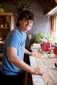 A high-school aged boy leans up against a work bench.