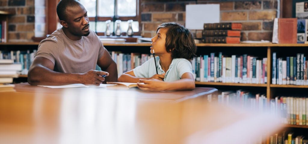 Teacher talking to a young student in a school library.