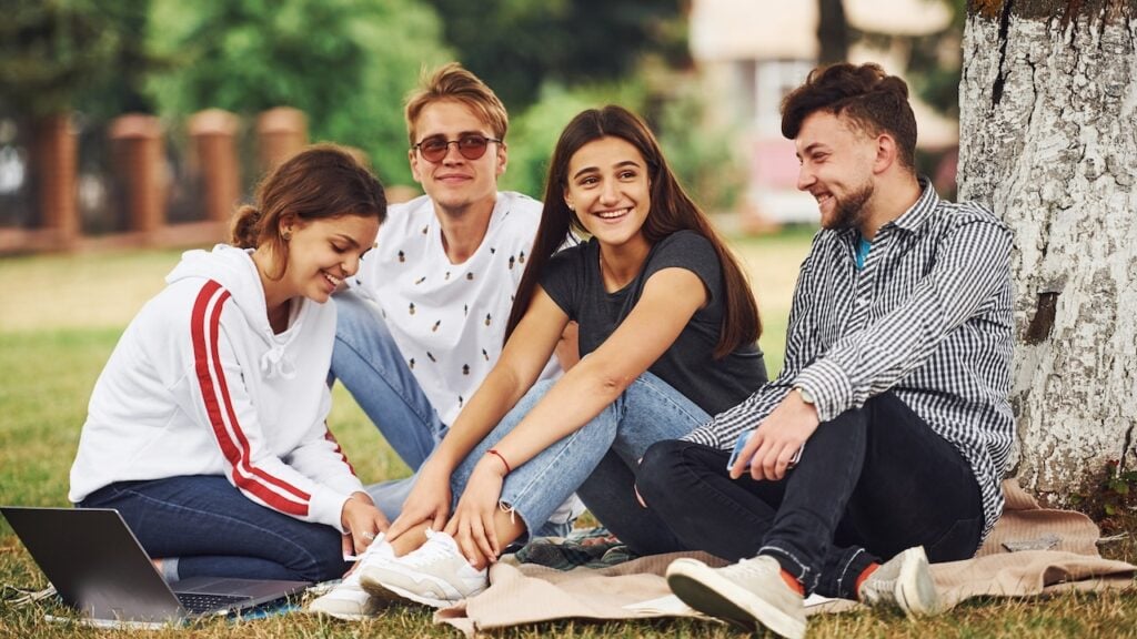 Group of young college students in casual clothes on green grass at daytime.